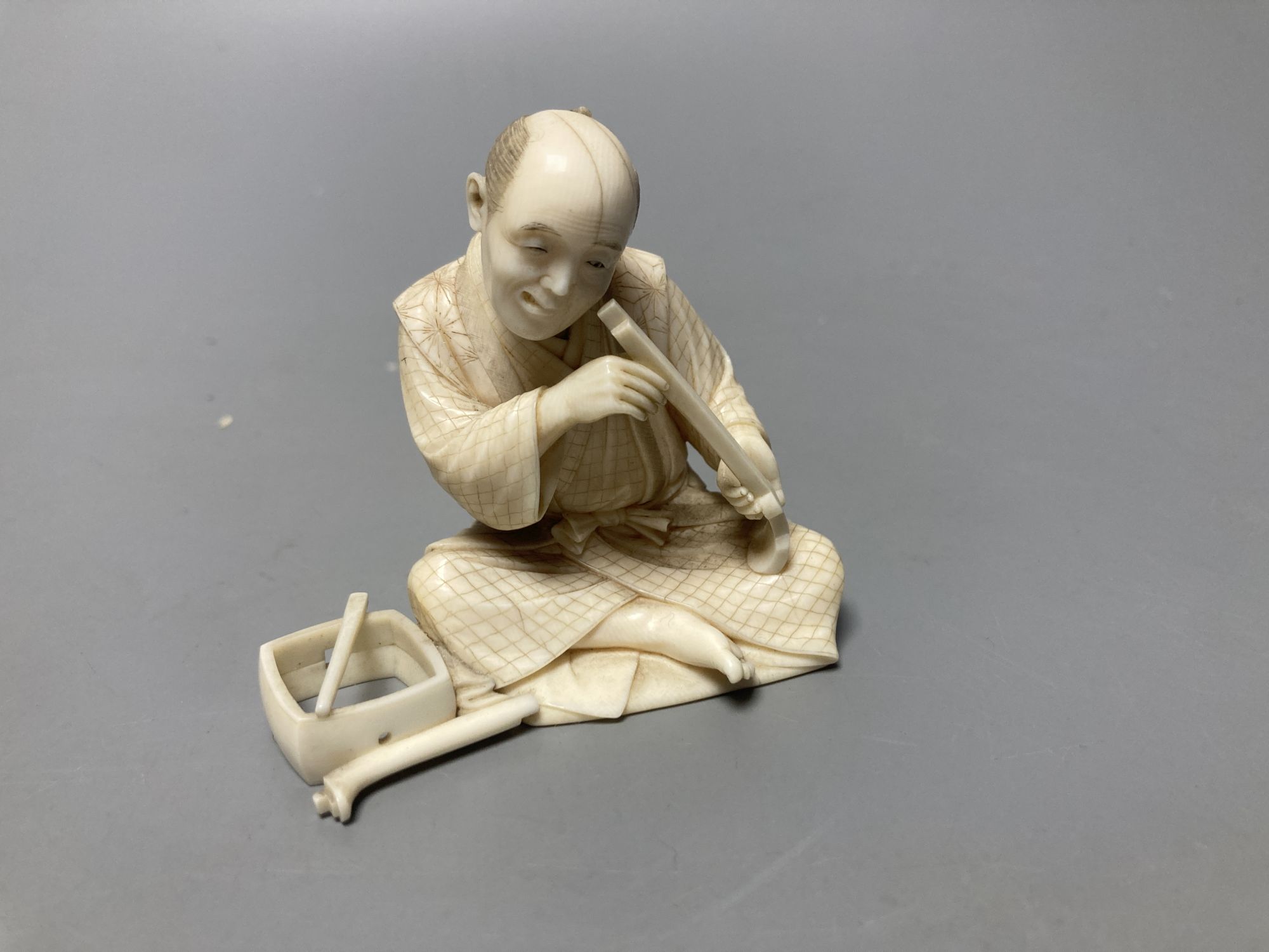 A Japanese ivory okimono of a furniture maker, signed tablet to base, Meiji period and a Chinese pierced ivory sleeve, height 6cm